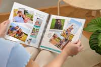 Scrapbook Pixum avec des photos de famille estivales Une femme qui tient dans sa main un scrapbook créatif dans lequel sont collées des photos de vacances et de famille.